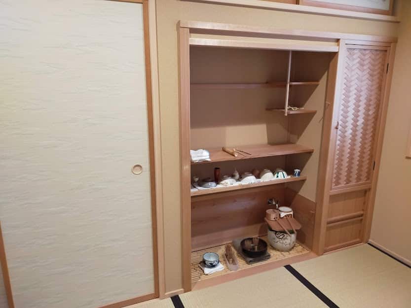 木製の棚に茶碗や茶器が収められた茶室の水屋の写真。