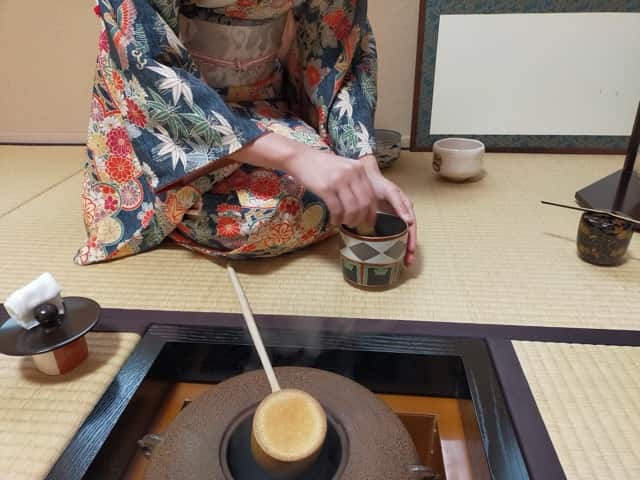 和服を着た女性が炉の前で茶道具を使い、お点前をしている様子。