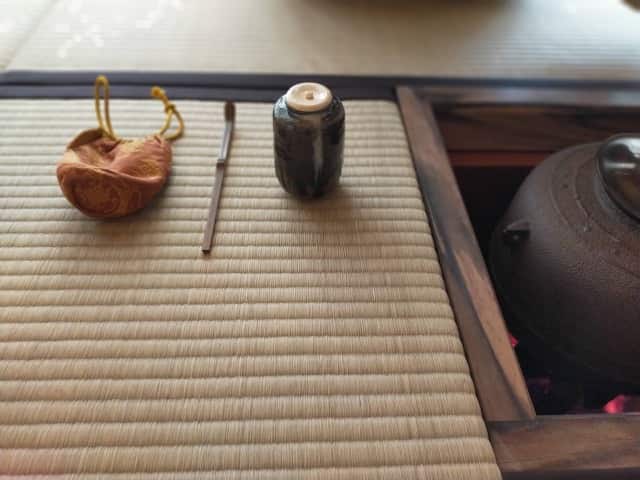 茶道の濃茶で拝見する御三器。茶入・茶杓・仕服が畳の上に並び、炭火の湯釜が静かに湯気を立てる。